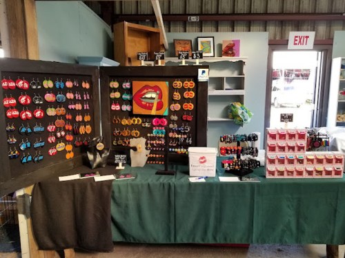 A colorful display of handmade earrings and accessories at a market stall, featuring various designs and prices.