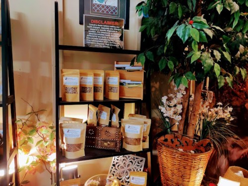 A display shelf with various packaged products, a disclaimer sign, and decorative plants and flowers.