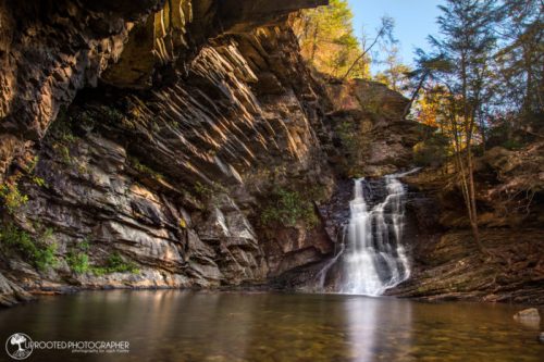 A serene waterfall cascades into a tranquil pool, surrounded by rocky cliffs and autumn foliage.