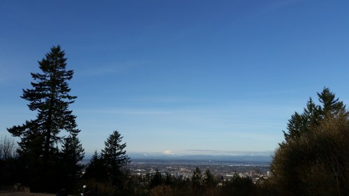 A scenic view of a clear blue sky over a landscape with trees and distant mountains.