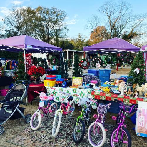 A festive outdoor market scene with colorful tents, holiday wreaths, toys, and bicycles for sale.