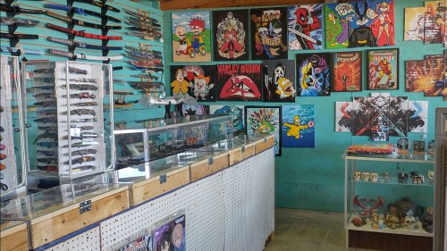 A colorful shop interior featuring display cases of knives and walls adorned with comic art and merchandise.