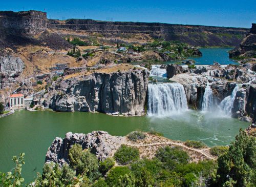 A scenic view of a waterfall cascading into a green river, surrounded by rocky cliffs and lush vegetation.