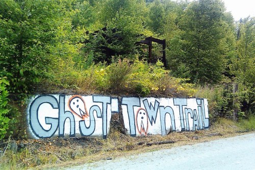 Graffiti on a wall reads "Ghost Town Trail," surrounded by greenery and trees.
