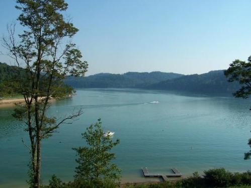 A serene lake surrounded by green hills, with a small boat on the water and a clear blue sky above.