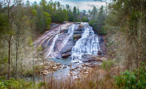 A scenic waterfall cascading over rocky cliffs, surrounded by lush green trees and a tranquil river below.