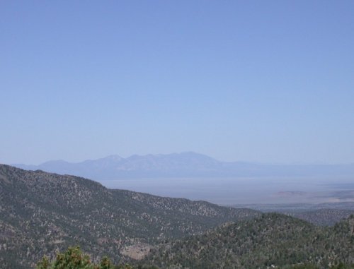 A panoramic view of distant mountains under a clear blue sky, with rolling green hills in the foreground.