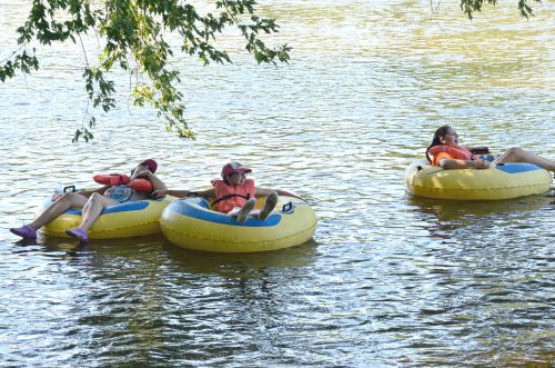 Three people relax on yellow inner tubes in a calm river, surrounded by trees and sunlight.