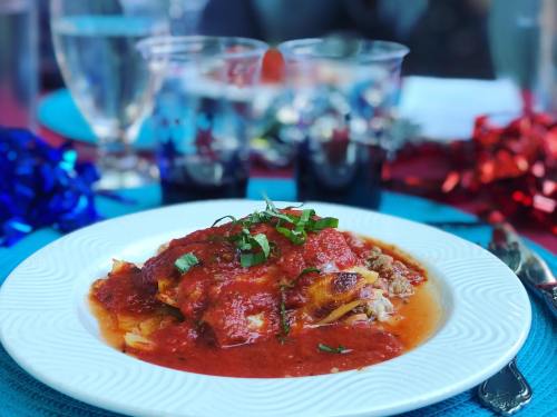 A plate of pasta topped with marinara sauce and fresh herbs, set on a colorful table with drinks in the background.