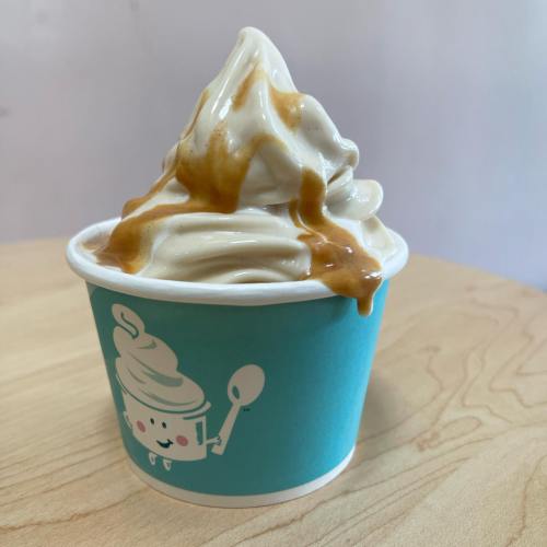 A cup of soft-serve ice cream topped with caramel sauce, sitting on a wooden table.