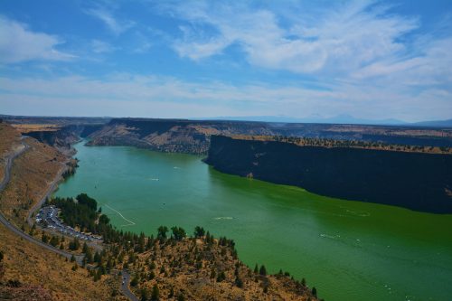 A scenic view of a green river winding through rocky cliffs under a blue sky with scattered clouds.