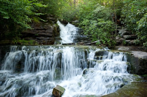 A serene waterfall cascading over rocks, surrounded by lush green foliage in a tranquil forest setting.