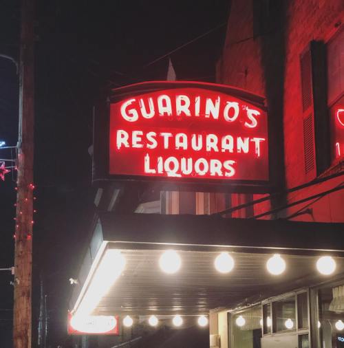 Neon sign for Guarino's Restaurant and Liquors illuminated at night.