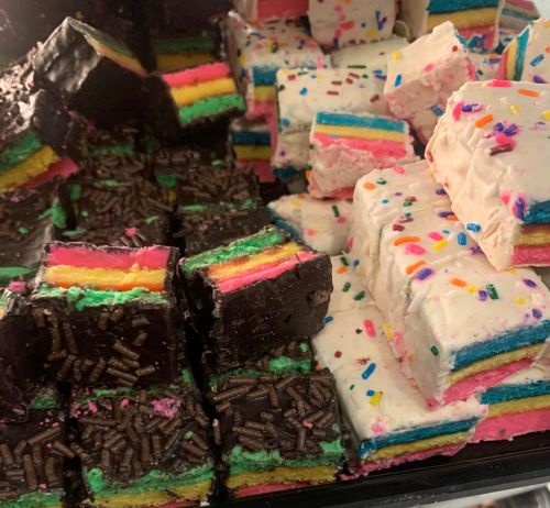 A colorful assortment of layered desserts with sprinkles and chocolate, featuring vibrant rainbow and white layers.