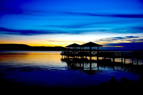 Silhouette of a pier at sunset, with vibrant blue and orange hues reflecting on calm water.
