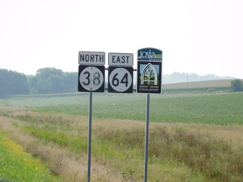 Road signs indicating North on Highway 38 and East on Highway 64, with a sign for Grant Wood Scenic Byway in Iowa.