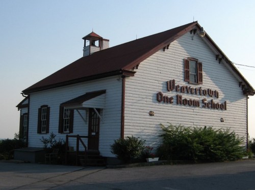 Historic one-room schoolhouse with a red roof and white wooden exterior, featuring "Weavertown One Room School" sign.