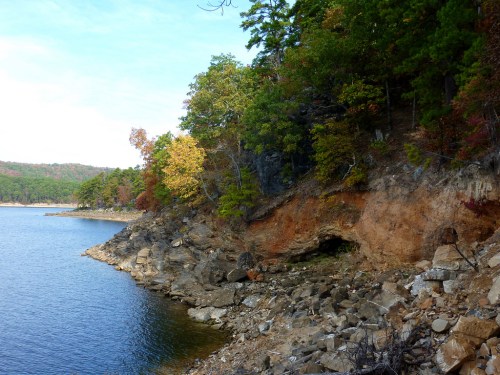 A serene lakeside scene with rocky shorelines and colorful autumn trees reflecting in the water.