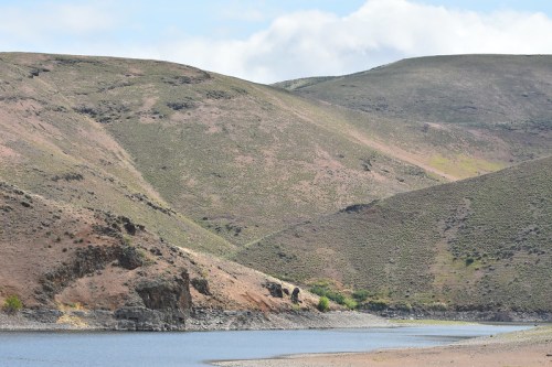 A serene landscape featuring rolling hills and a calm body of water under a partly cloudy sky.
