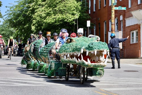 A colorful, large crocodile-themed float with people in costumes riding through a street during a parade.