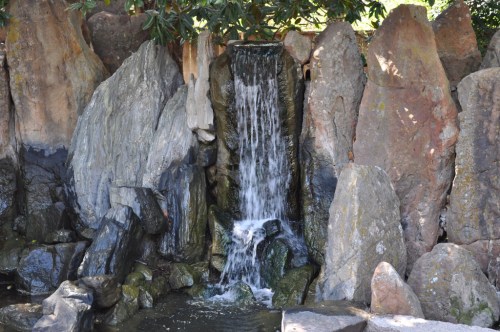 A small waterfall cascading over rocks into a serene pool, surrounded by natural stone formations.