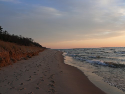 A serene beach at sunset, with footprints in the sand and gentle waves lapping at the shore.