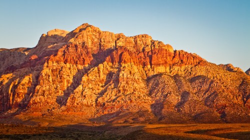 Sunset casts warm hues on rugged red rock formations in a desert landscape.
