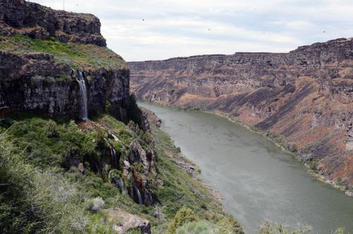 A scenic view of a river winding through a canyon, with a waterfall cascading from a rocky cliffside.