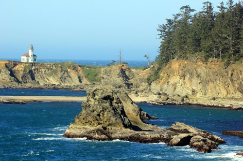 A scenic coastal view featuring a lighthouse, rocky formations, and lush greenery along the shoreline.