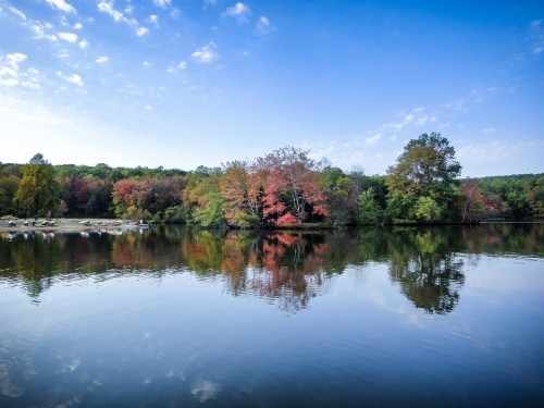 A serene lake reflecting colorful autumn trees under a clear blue sky.