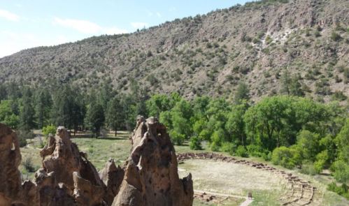 A scenic view of rocky formations overlooking a green valley with trees and a circular stone arrangement.