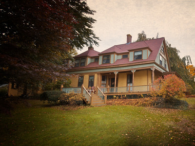 A large, two-story yellow house with a red roof, surrounded by trees and autumn foliage.