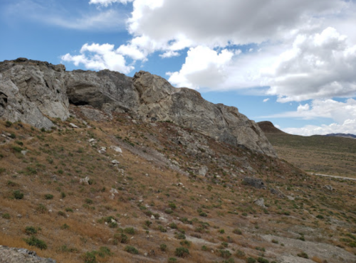 Rocky hillside with sparse vegetation under a partly cloudy blue sky.