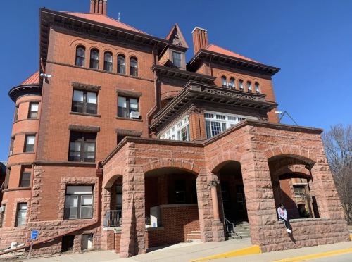 Historic red brick building with a large porch and multiple gabled roofs under a clear blue sky.
