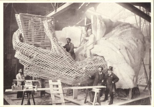 Historic photo of men working on a large sculpture, featuring a hand structure made of wood and fabric in a workshop.