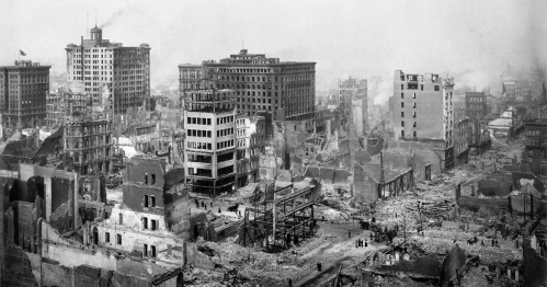 A black-and-white photo of a devastated cityscape with ruined buildings and debris after a disaster.