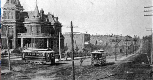 Historic black-and-white photo of a streetcar at a junction near a large Victorian-style house.