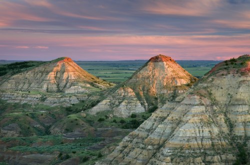 Sunset over layered hills with peaks, showcasing vibrant colors and a vast landscape in the background.