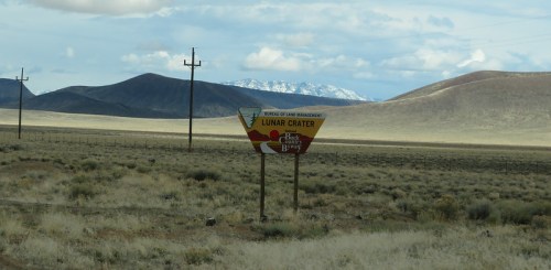 Sign for Lunar Crater in a vast, arid landscape with mountains in the background under a cloudy sky.