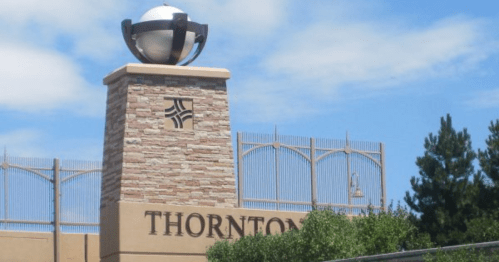 Sign for Thornton featuring a stone pillar and a globe sculpture against a blue sky. Green foliage in the foreground.