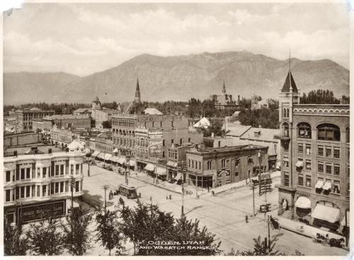 Historic view of Ogden, Utah, featuring buildings, streets, and the Wasatch Range in the background.