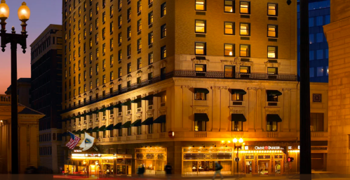Historic hotel building illuminated at dusk, featuring large windows and a welcoming entrance.
