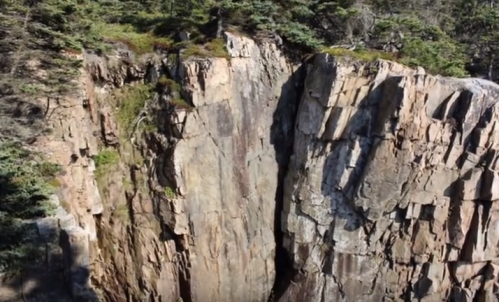 Aerial view of a steep rock cliff surrounded by trees, showcasing rugged terrain and natural beauty.