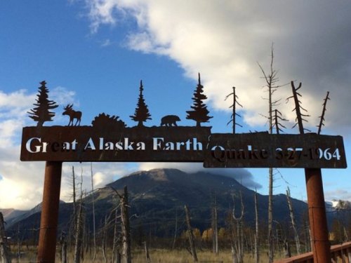 Sign commemorating the Great Alaska Earthquake of 1964, with silhouettes of wildlife and trees against a cloudy sky.