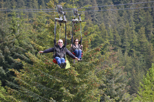 Two people on a chairlift ride above lush green trees, enjoying a scenic view in a mountainous area.