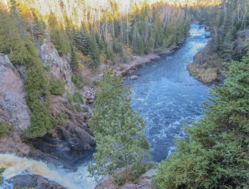 A scenic view of a river winding through a forested landscape with rocky banks and autumn foliage.
