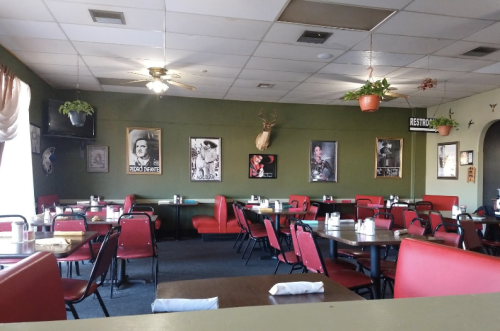 Interior of a restaurant featuring red chairs, green walls, and framed photos, with tables set for dining.