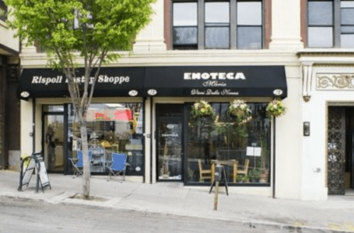A storefront with a black awning reading "Enoteca" and "Rispol's Pasta Shoppe," featuring outdoor seating and plants.