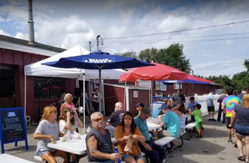 A lively outdoor scene at a beer garden with people sitting at tables under colorful umbrellas.