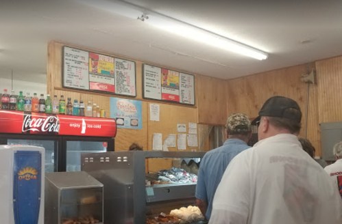 A busy diner with a menu board, customers in line, and a display of drinks and food items.